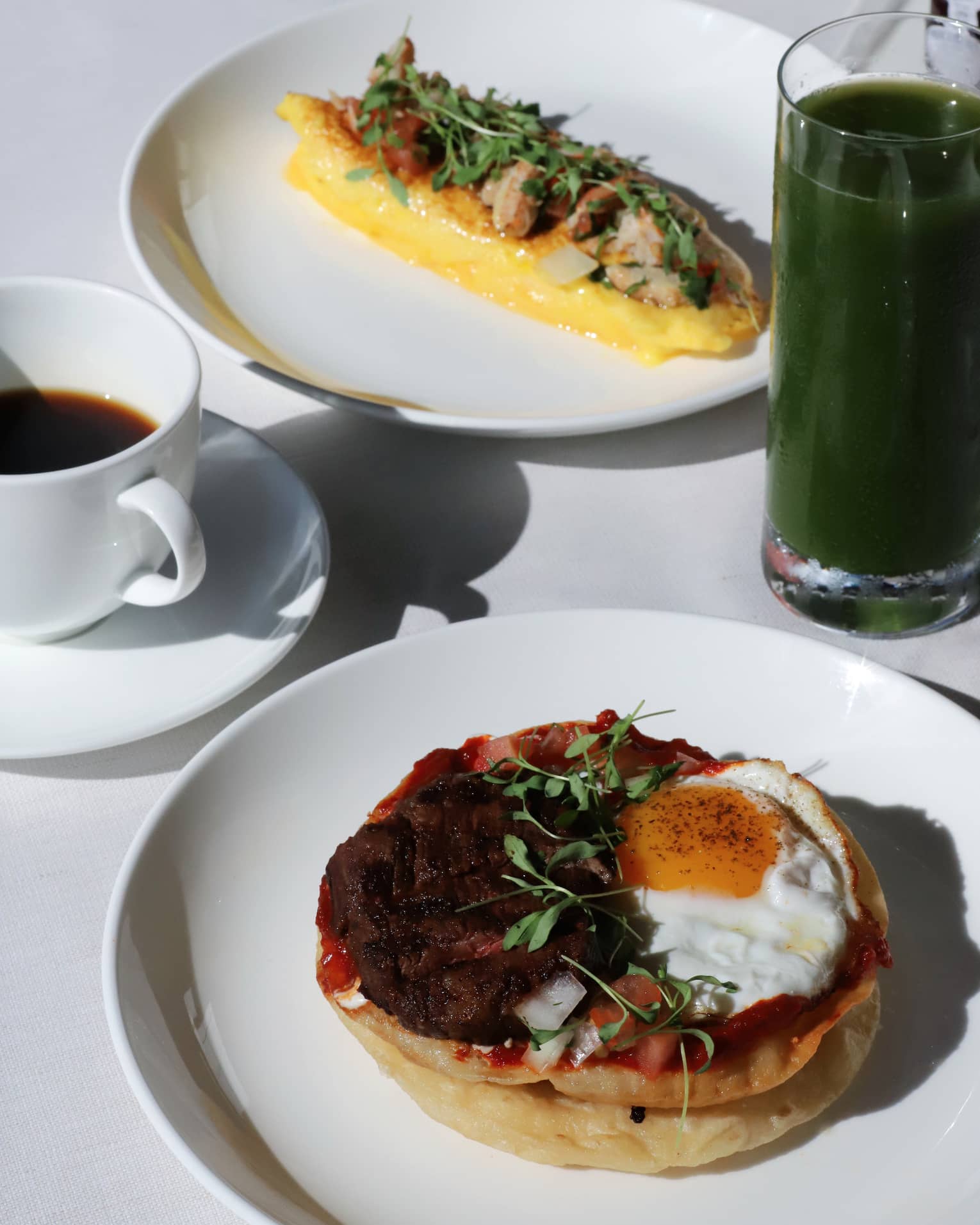Close up of a table filled with breakfast dishes, green juice and coffee