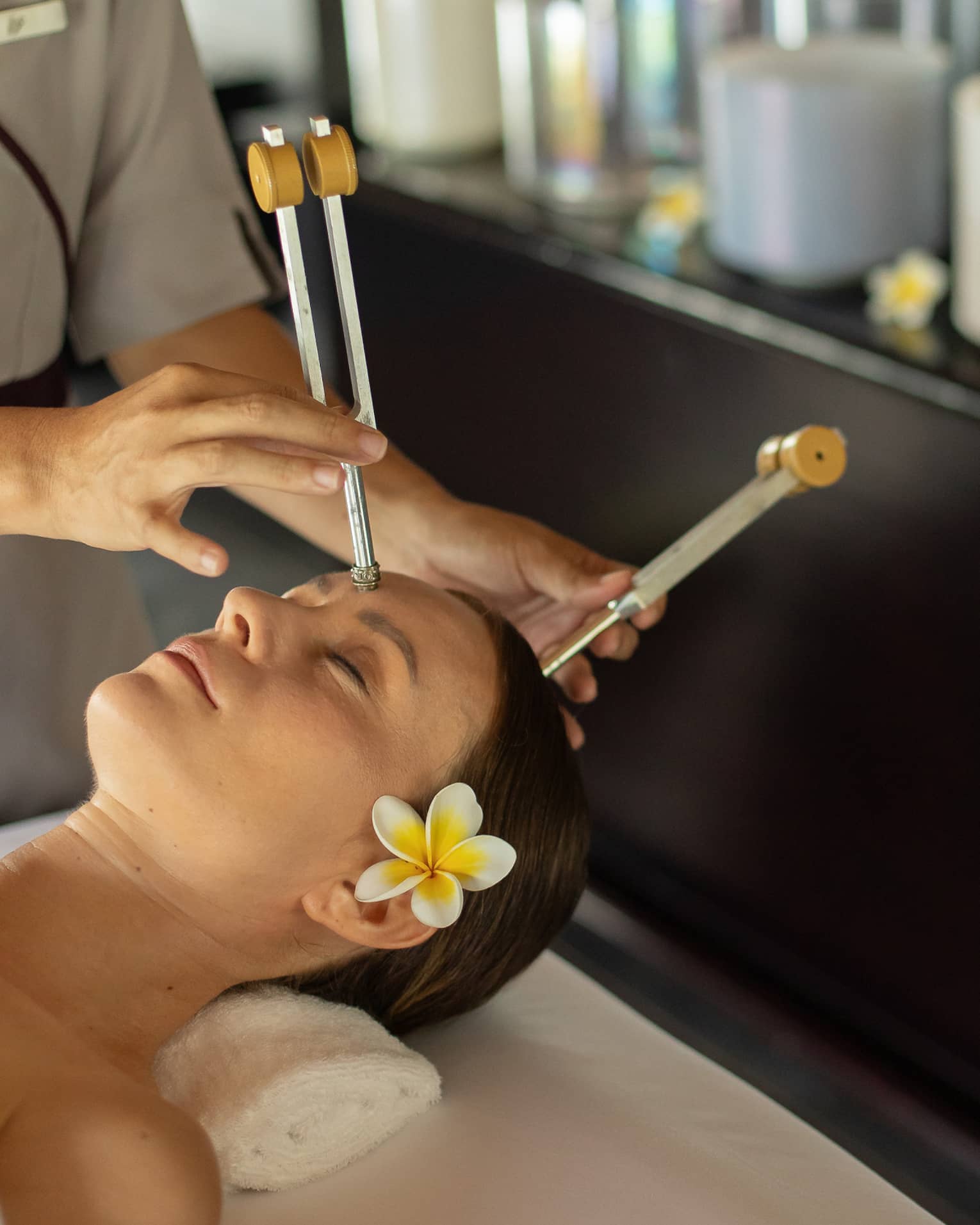 A practitioner delicately applies ohm tuning forks to the forehead and crown of a guest resting peacefully on a massage bed.