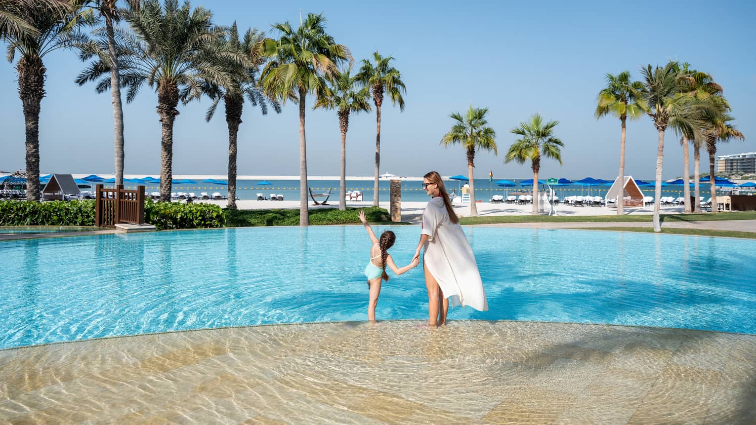 A woman and a little girl hold hands while wading in the outdoor pool overlooking the Arabian Gulf