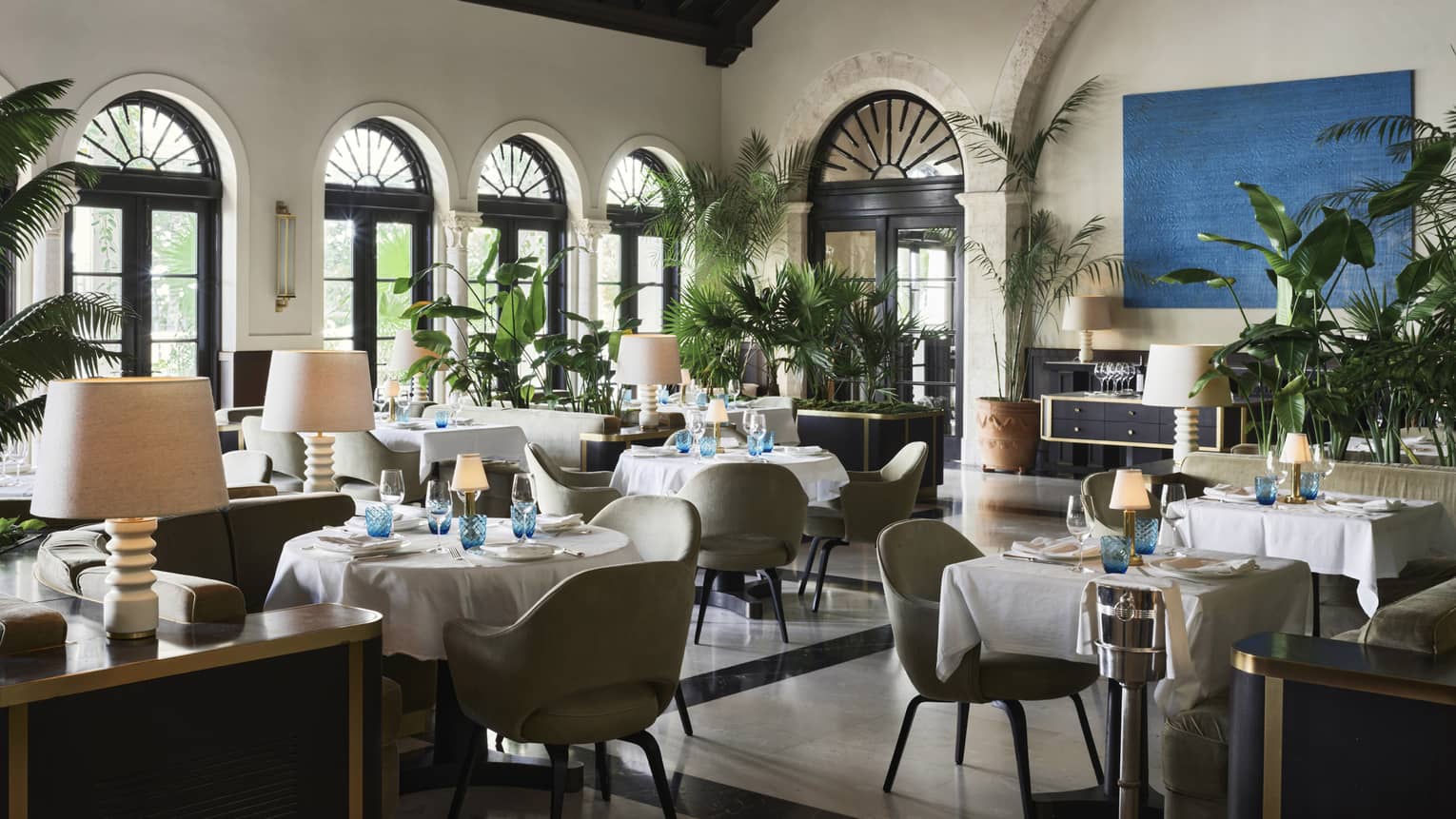 restaurant on lido The inside of a restaurant with white linen cloth on tables, a large chandelier and beige walls.
