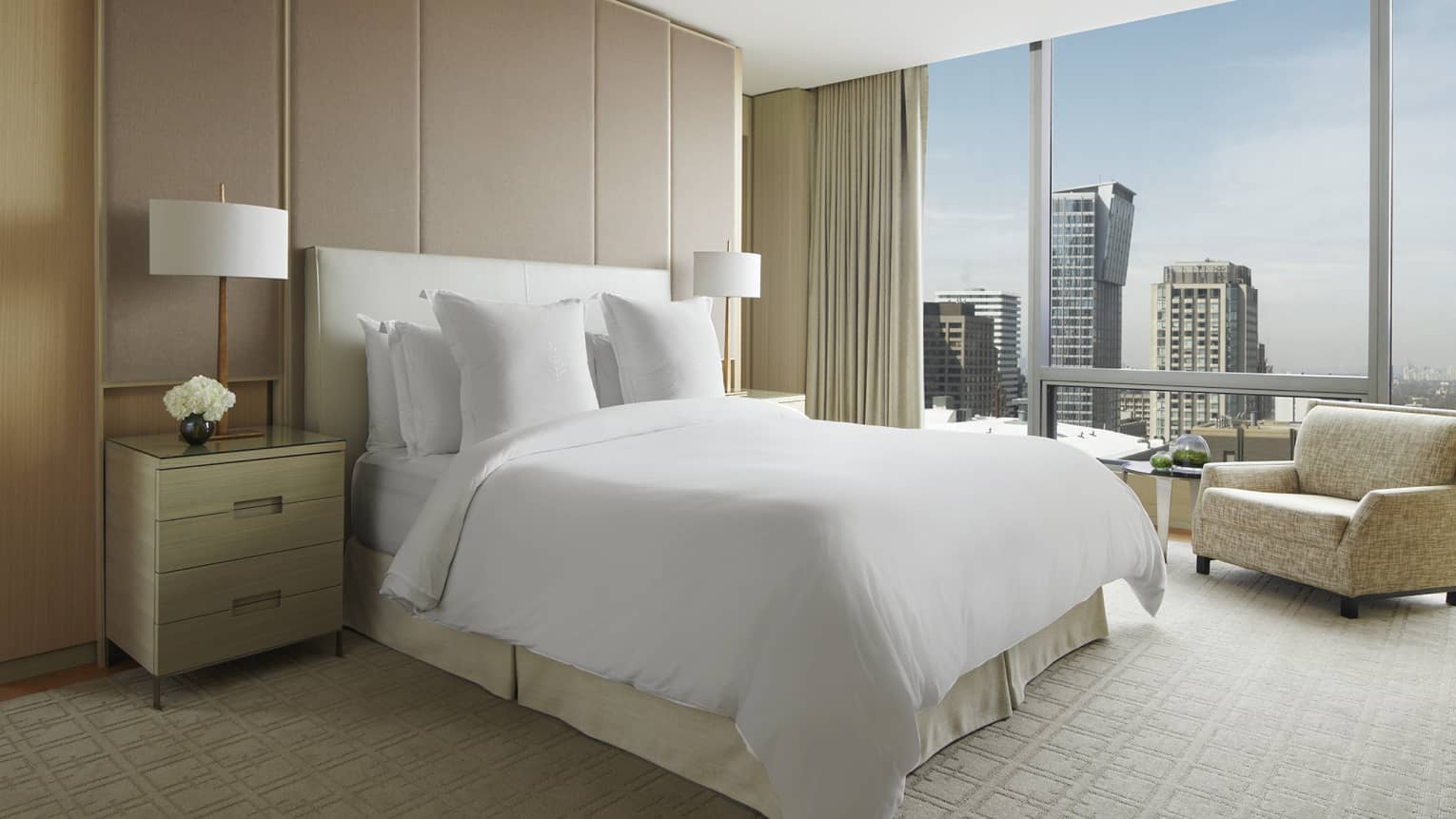 Royal Suite with white king bed, tan carpet and armchair, floor-to-ceiling window with views of downtown Toronto