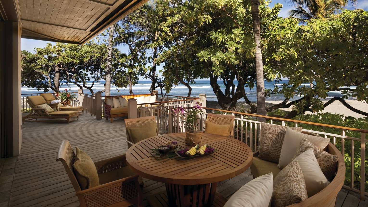 Kailani Suite round wood patio table, cushioned chairs on deck by trees
