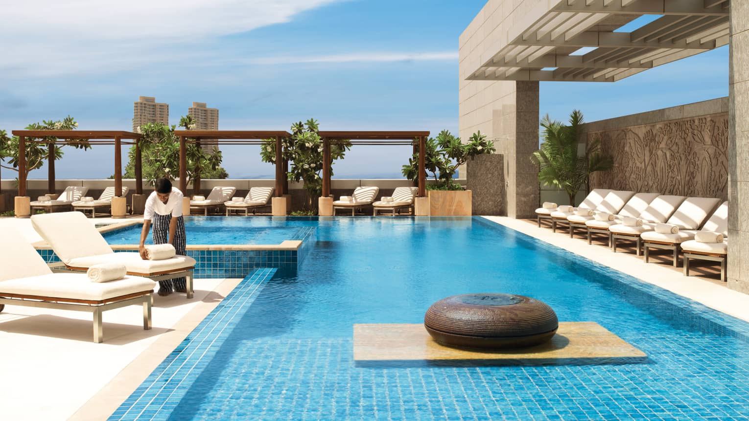 Hotel staff sets rolled white towel on lounge chair by sunny outdoor swimming pool