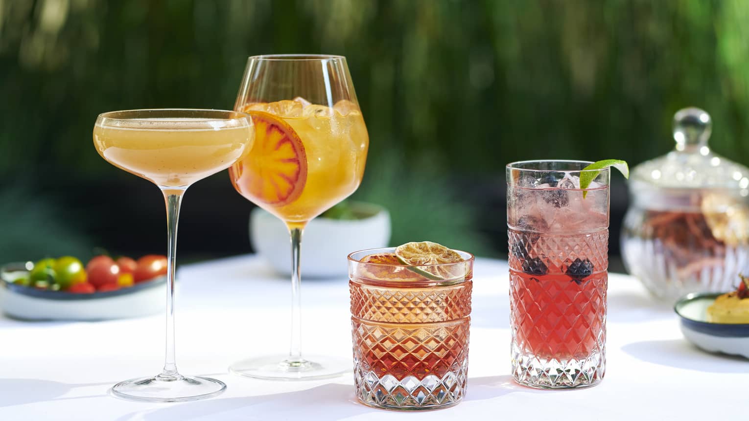 A variety of cocktails on a white table that are orange or red in colour.
