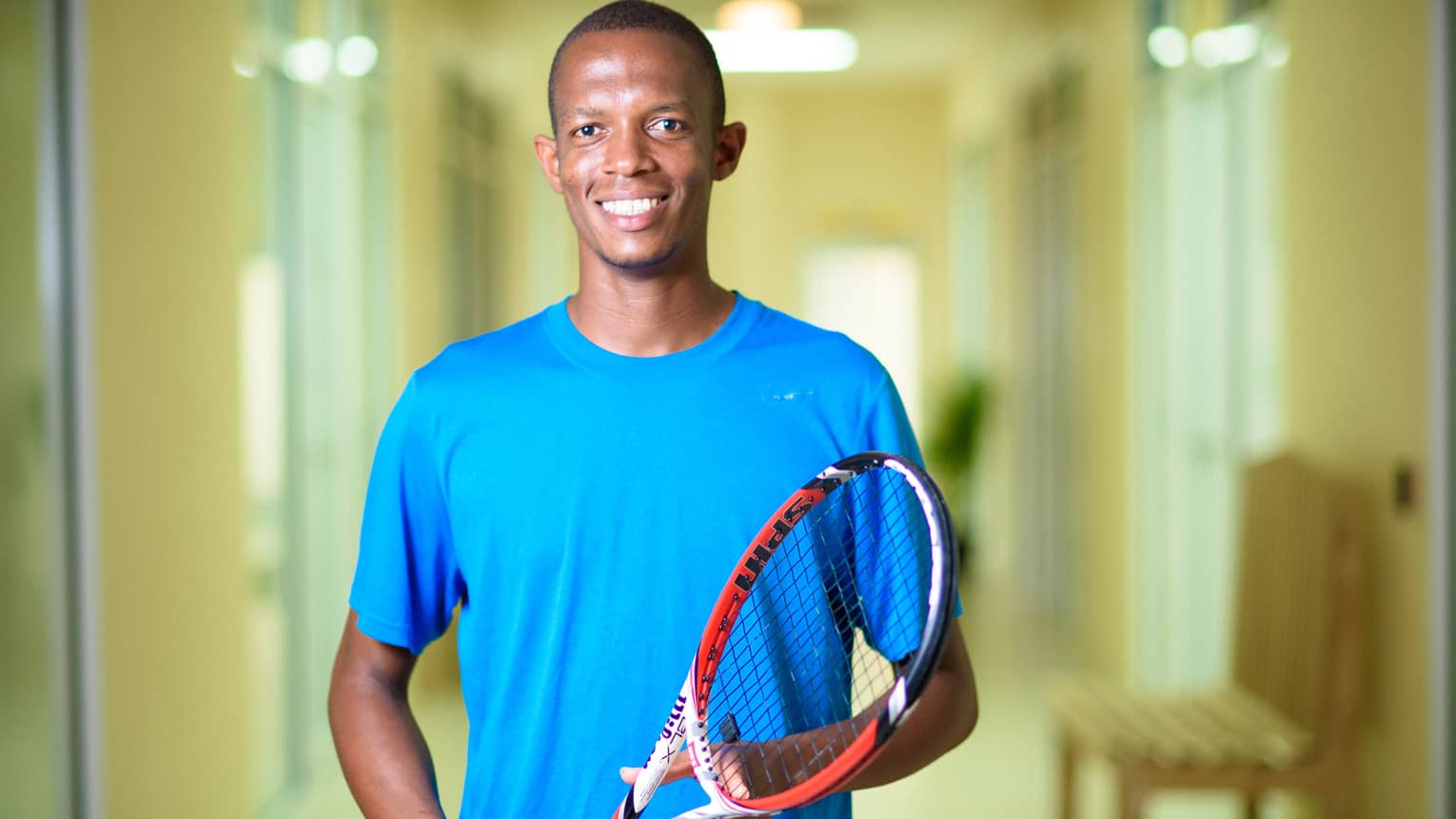 Smiling man in blue shirt holds red tennis racket