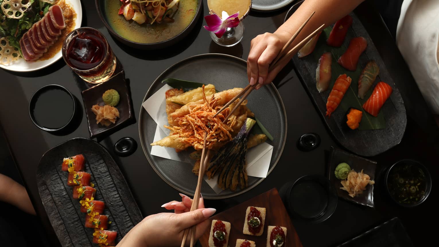 Vegetable tempura set in the centre of a black table filled with sushi dishes