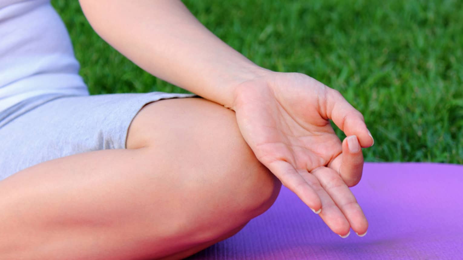 Side of hand, leg in cross legged meditation pose on yoga mat 