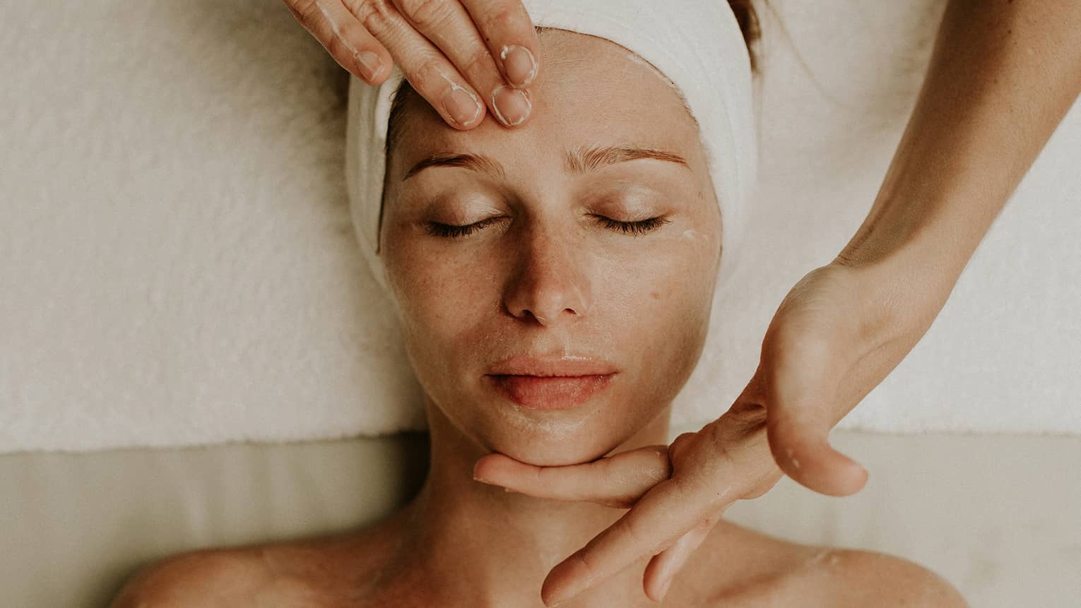 Person receiving a relaxing facial massage with eyes closed and head wrapped in a towel