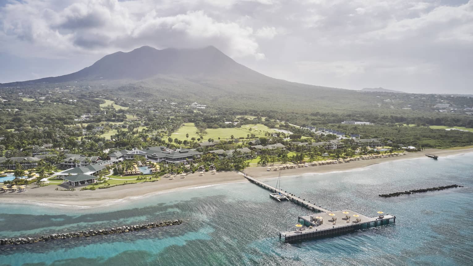 Aerial view of a resort property and dock on a beach shore with a mountain in the distance.