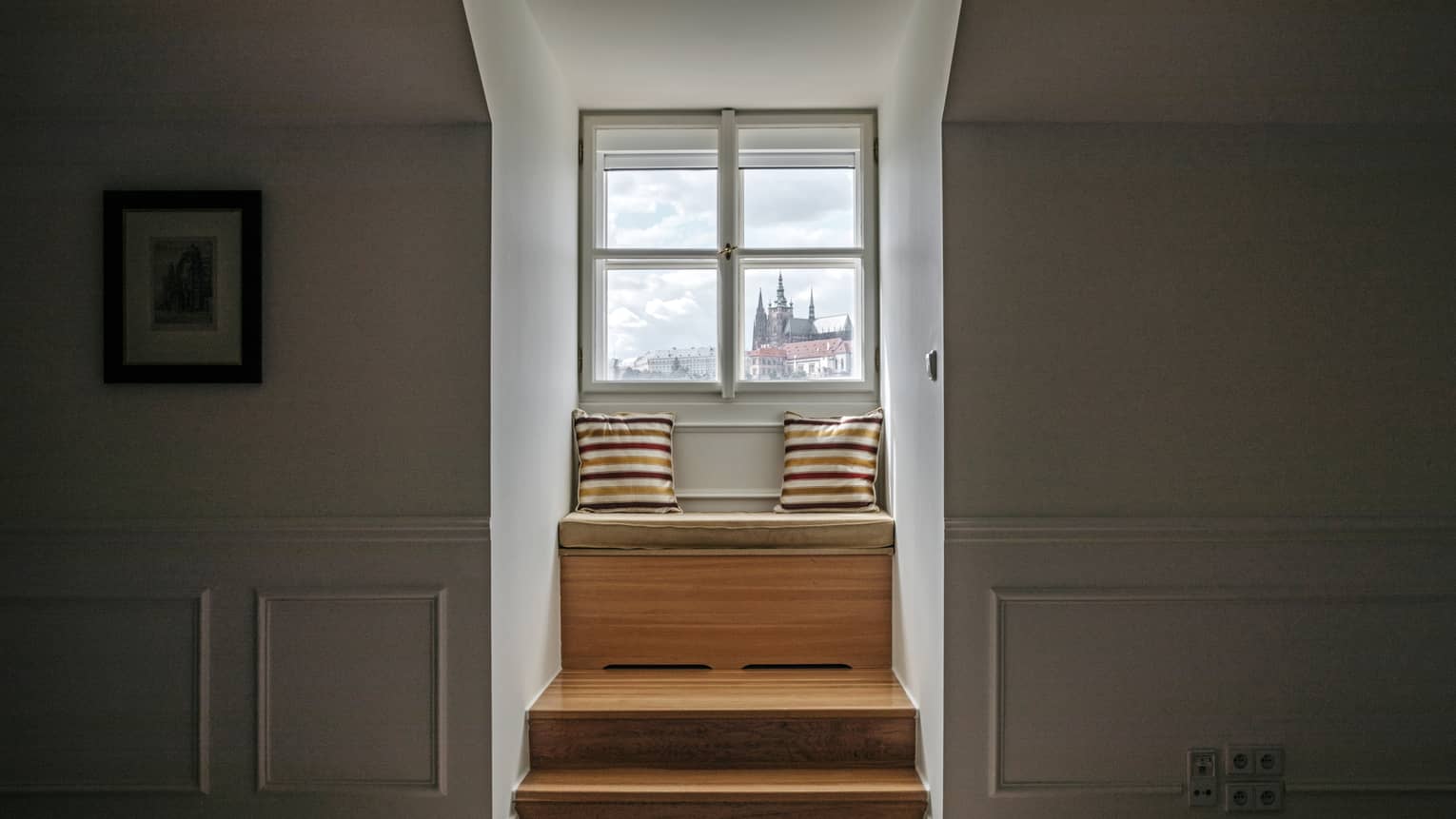 Wooden steps up to window seat dressed with two striped pillows by window with castle view