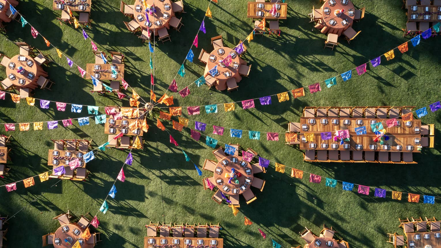 Many dining tables and chairs set up with colourful streamer decorations above it.
