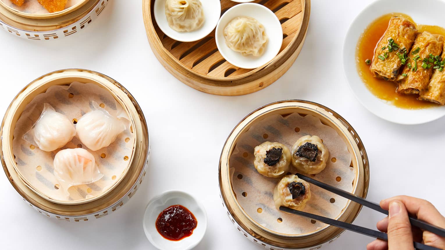 Aerial shot of Dim Sum selection, man reaching for dumplings steamer basket with chopsticks