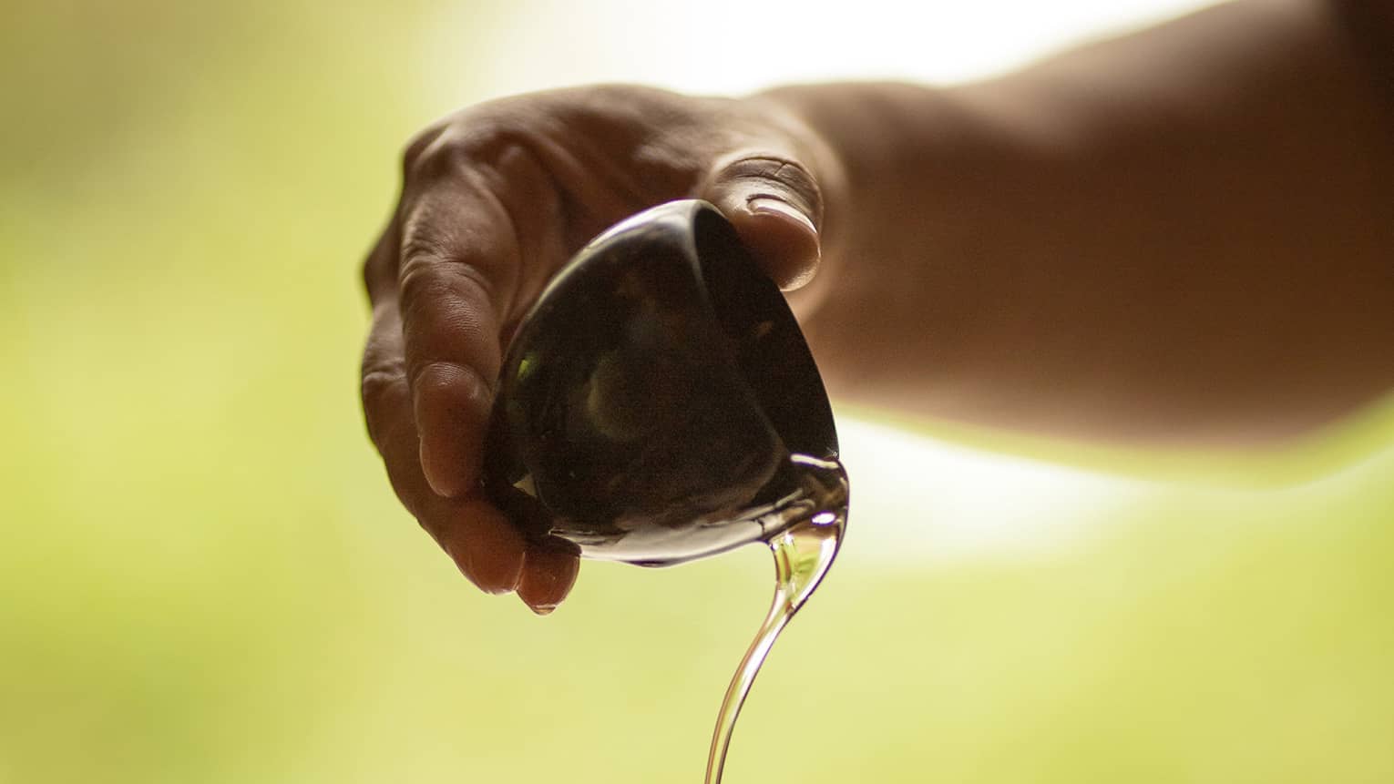 A set of hands pours massage oil from a ceramic bowl into a palm