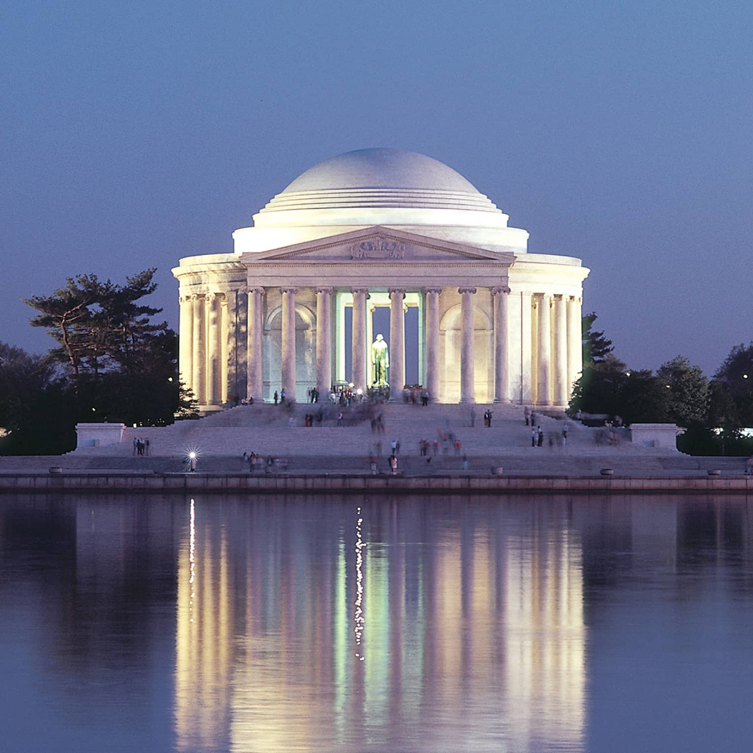A large historical monument of white pillars and a large dome next to water.
