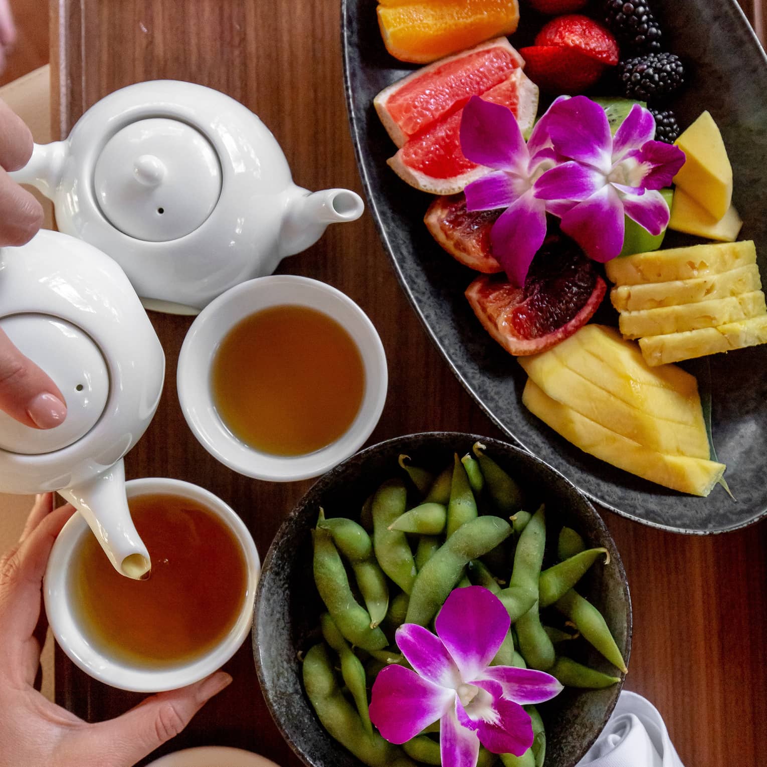 Fresh fruit, edamame and tea on a wooden platter
