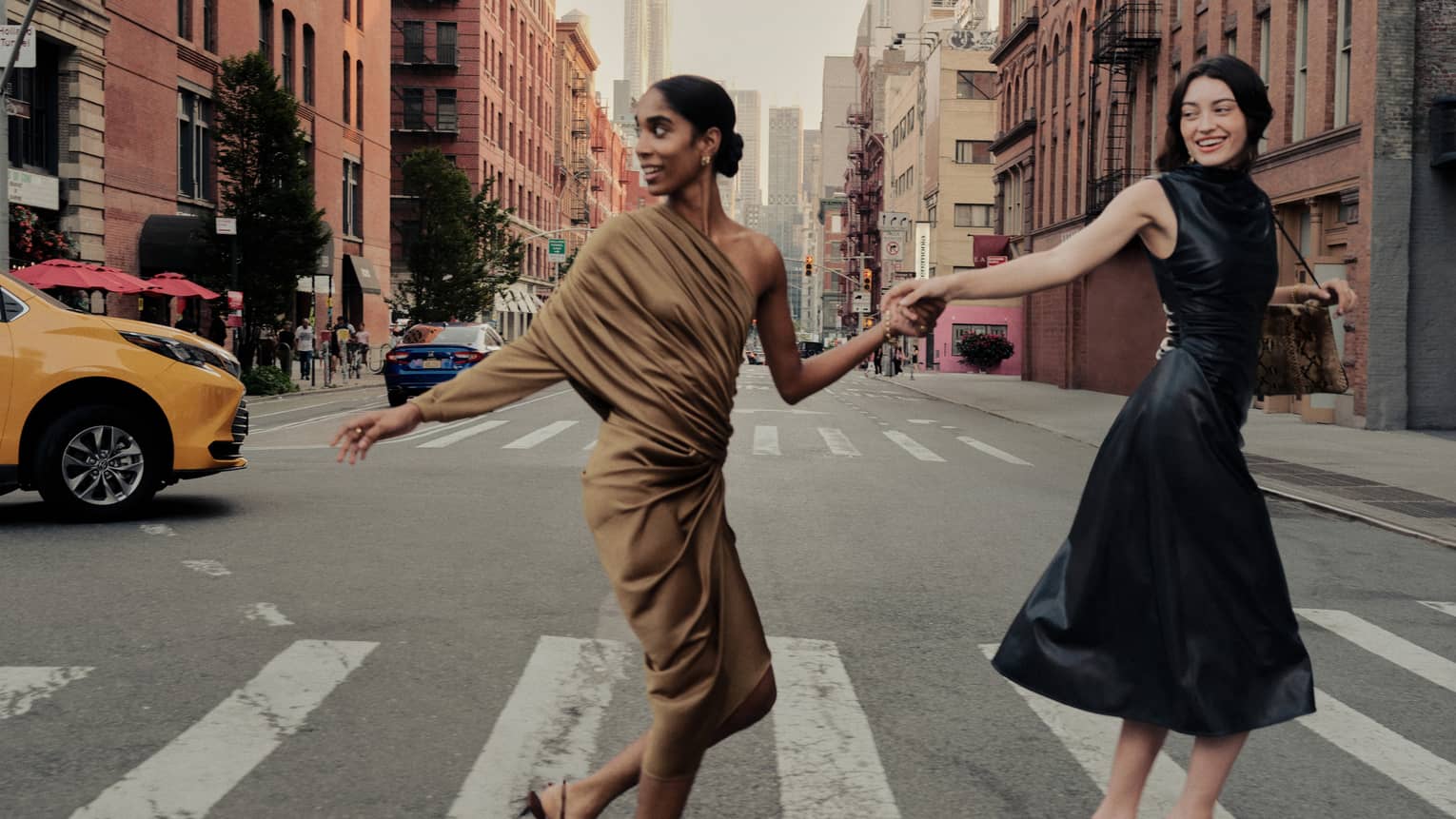 Two women holding hands cross a street in New York City.