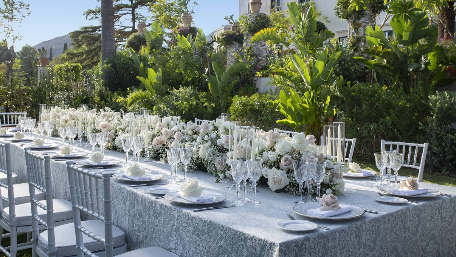 Elegantly set long table with extended floral wedding centrepiece alongside lush garden wall