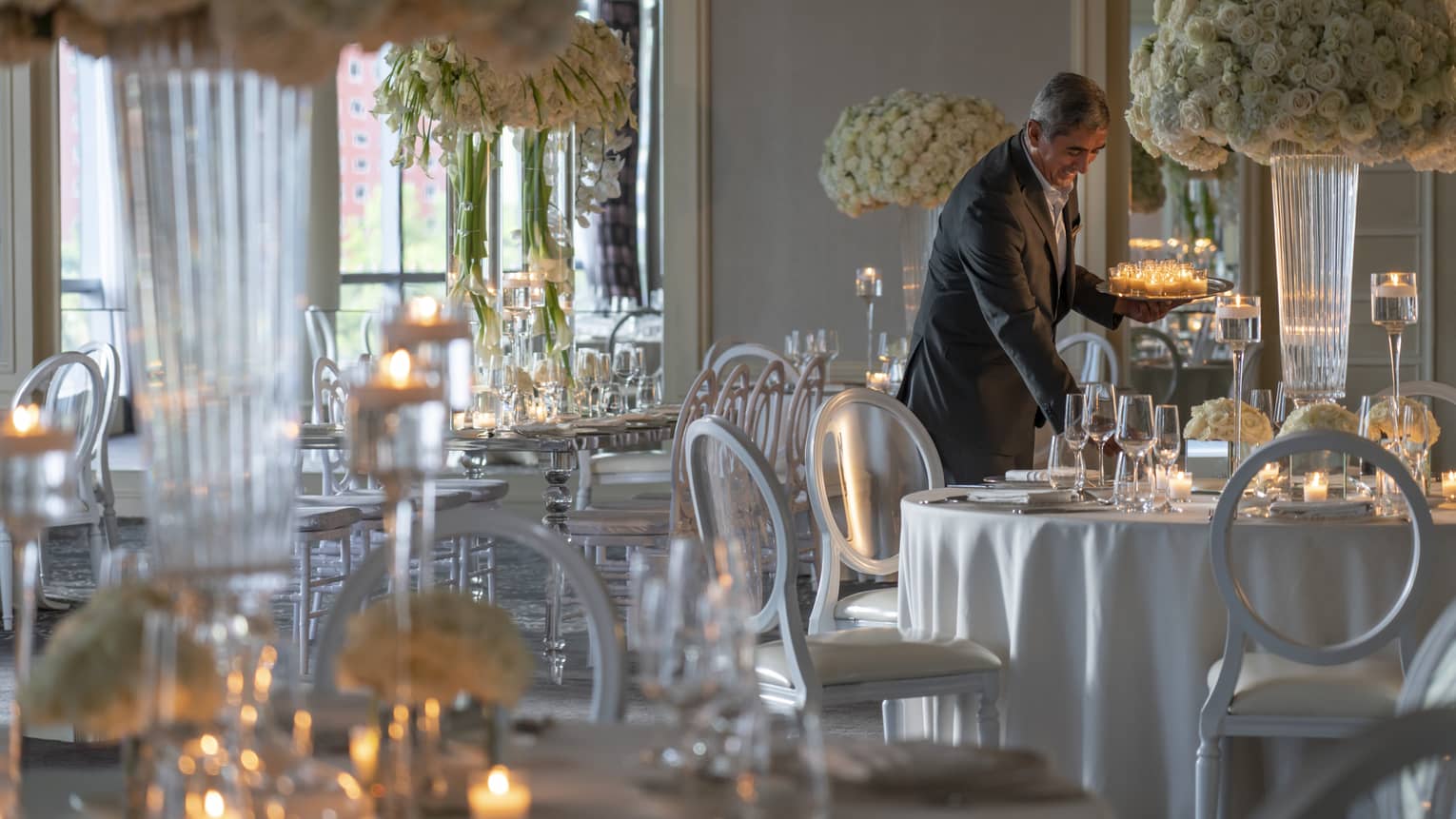 Smiling hotel staff sets tea light candles on round banquet tables in ballroom