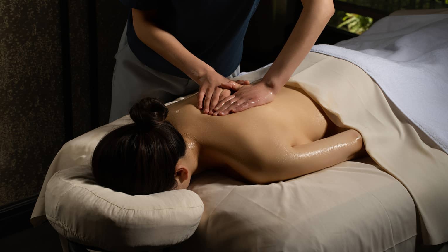 Person lying face down and covered in a beige sheet getting a massage