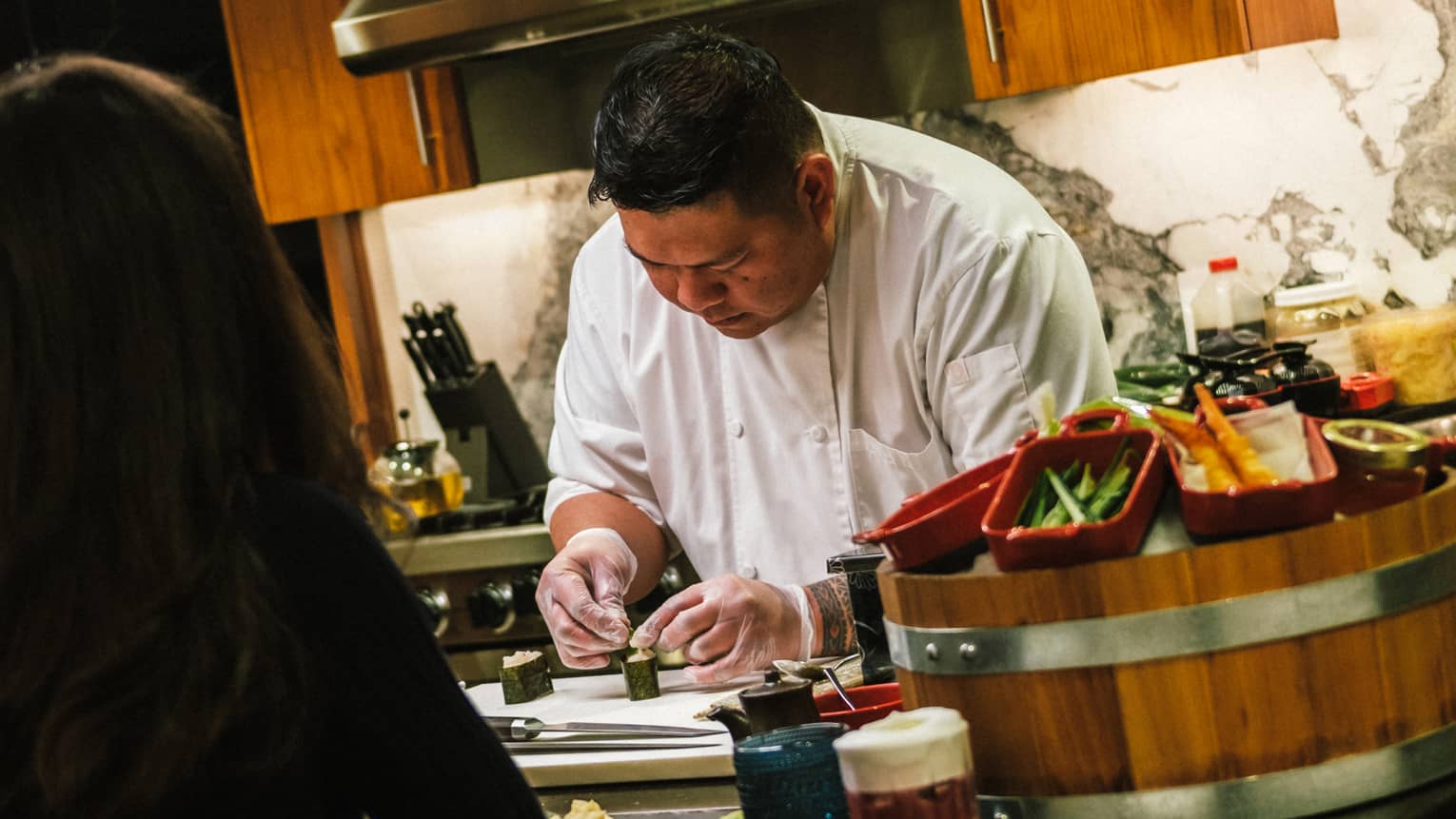 Chef Jaime Magadia preparing a sushi roll in a kitchen with guest watching