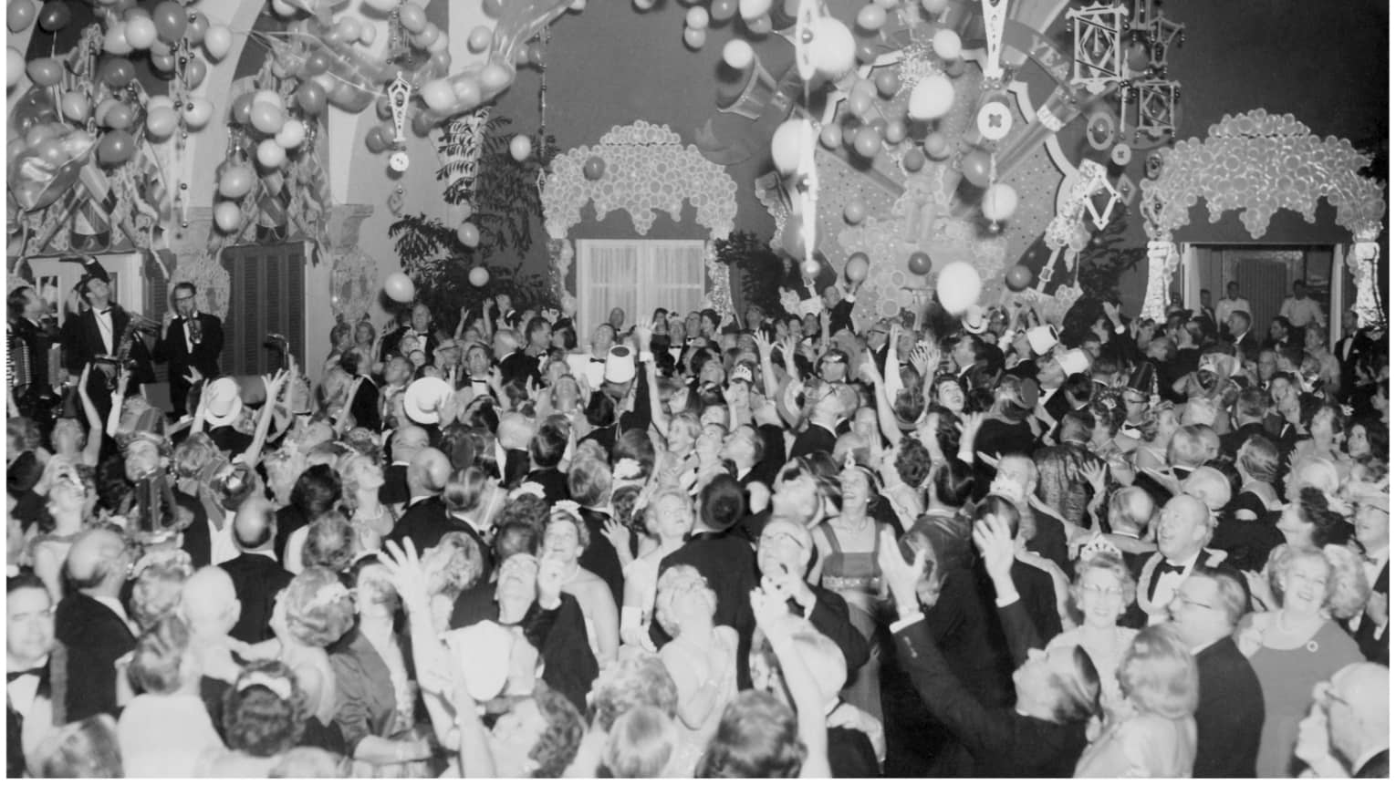 A black and white photo of a large group of people celebrating with balloons in a large room.