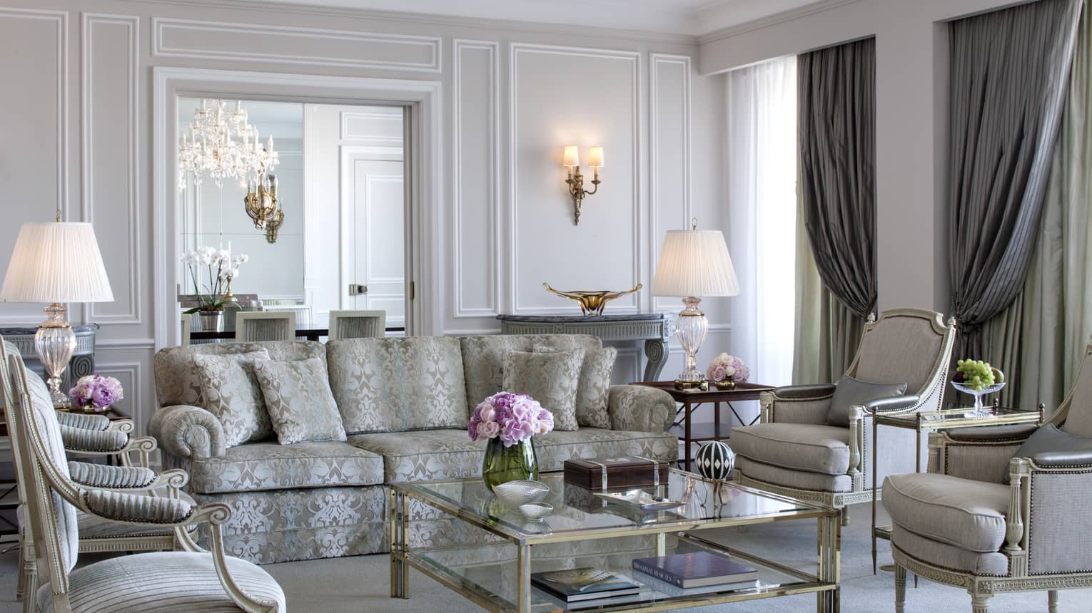 Royal Suite bright, elegant living room with blue-and-grey satin sofa, armchairs, glass coffee table with gold trim, white walls