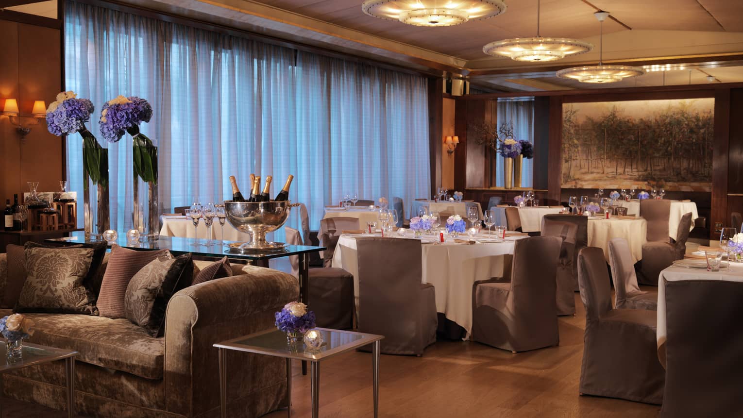 Il Teatro, plush sofa, table with Champagne bottles and flowers in front of dining tables 