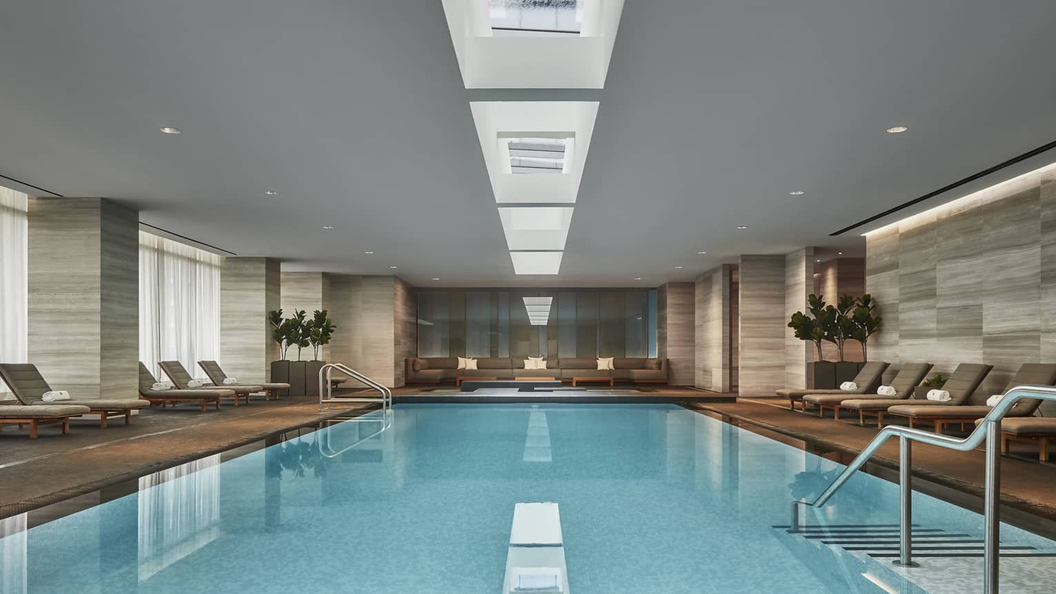 A long pool with a gentle sloping staircase that enters the water. Several lounge chairs surround the pool. 