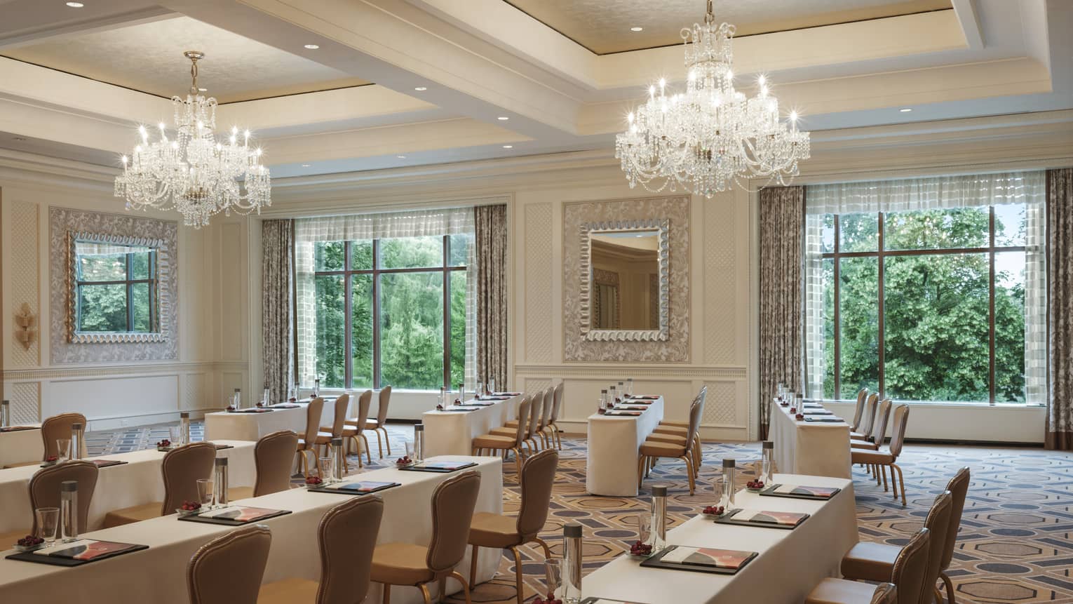 Rows of meeting tables and chairs under crystal chandelier in large ballroom