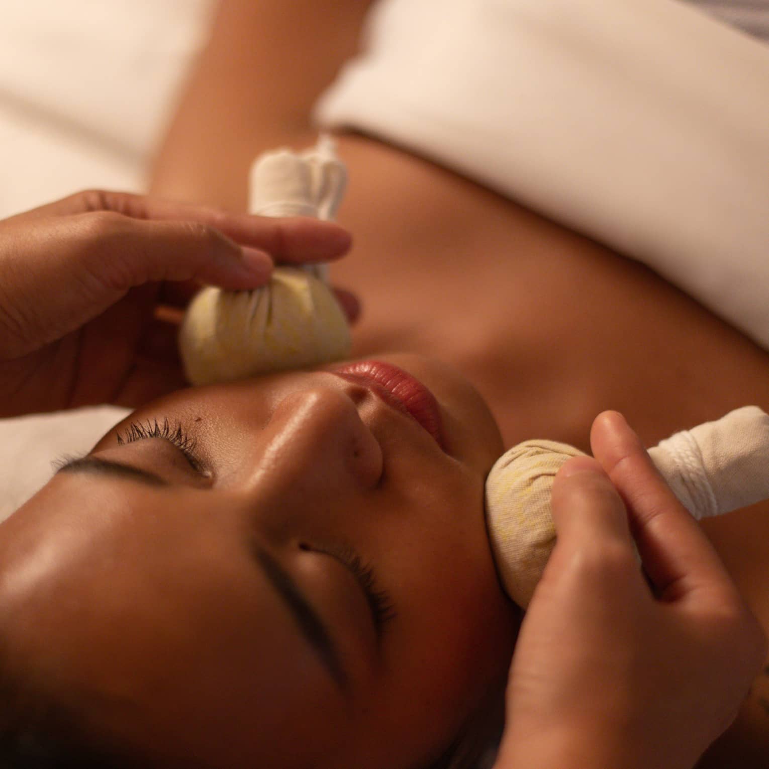 Therapist applies Thai herbal compresses to either side of woman?s face