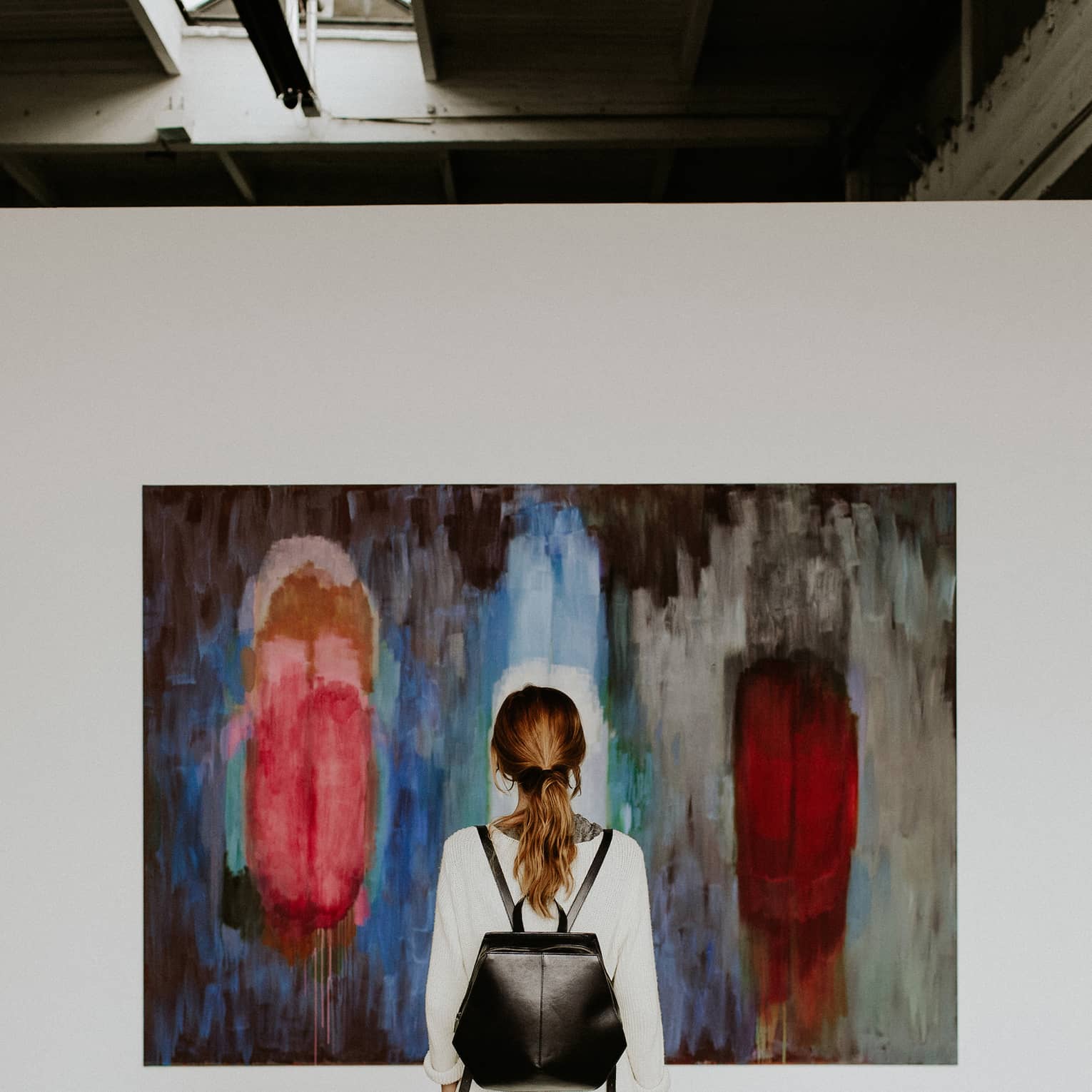A person with a backpack standing in front of an abstract painting in an art gallery.
