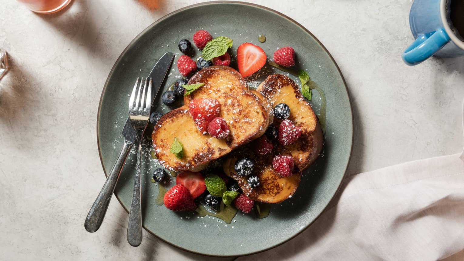 French toast with blueberries and strawberries on a teal plate.