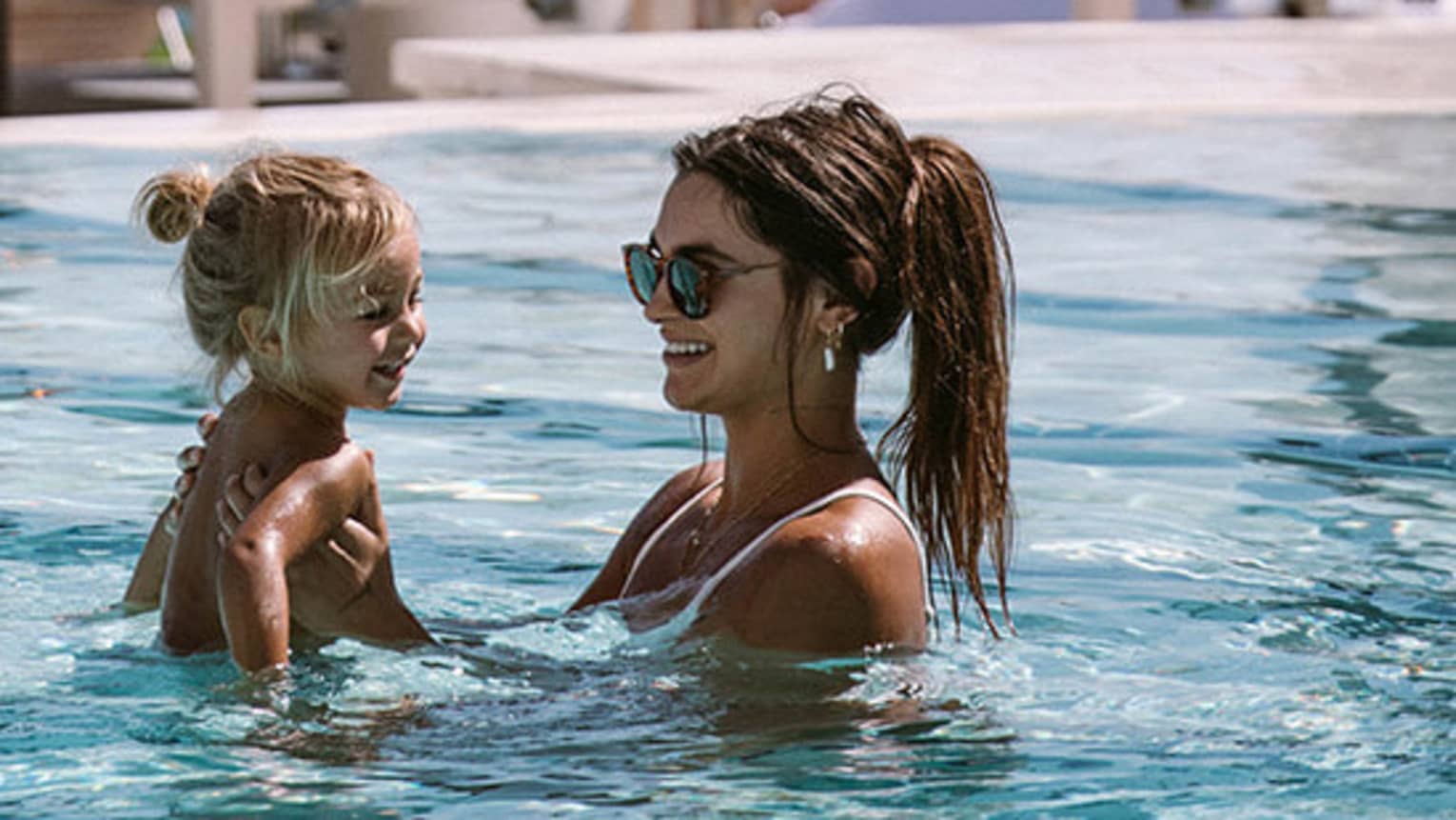 Adult and holds a young shild in a pool, both smiling