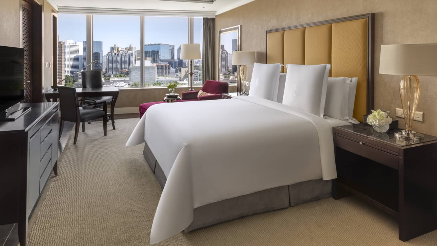 Hotel room with king bed, tan headboard, desk with two chairs, dresser and window-side chaise