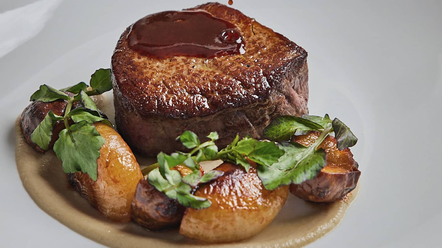 A filet of steak with potatoes and herbs on a white plate.