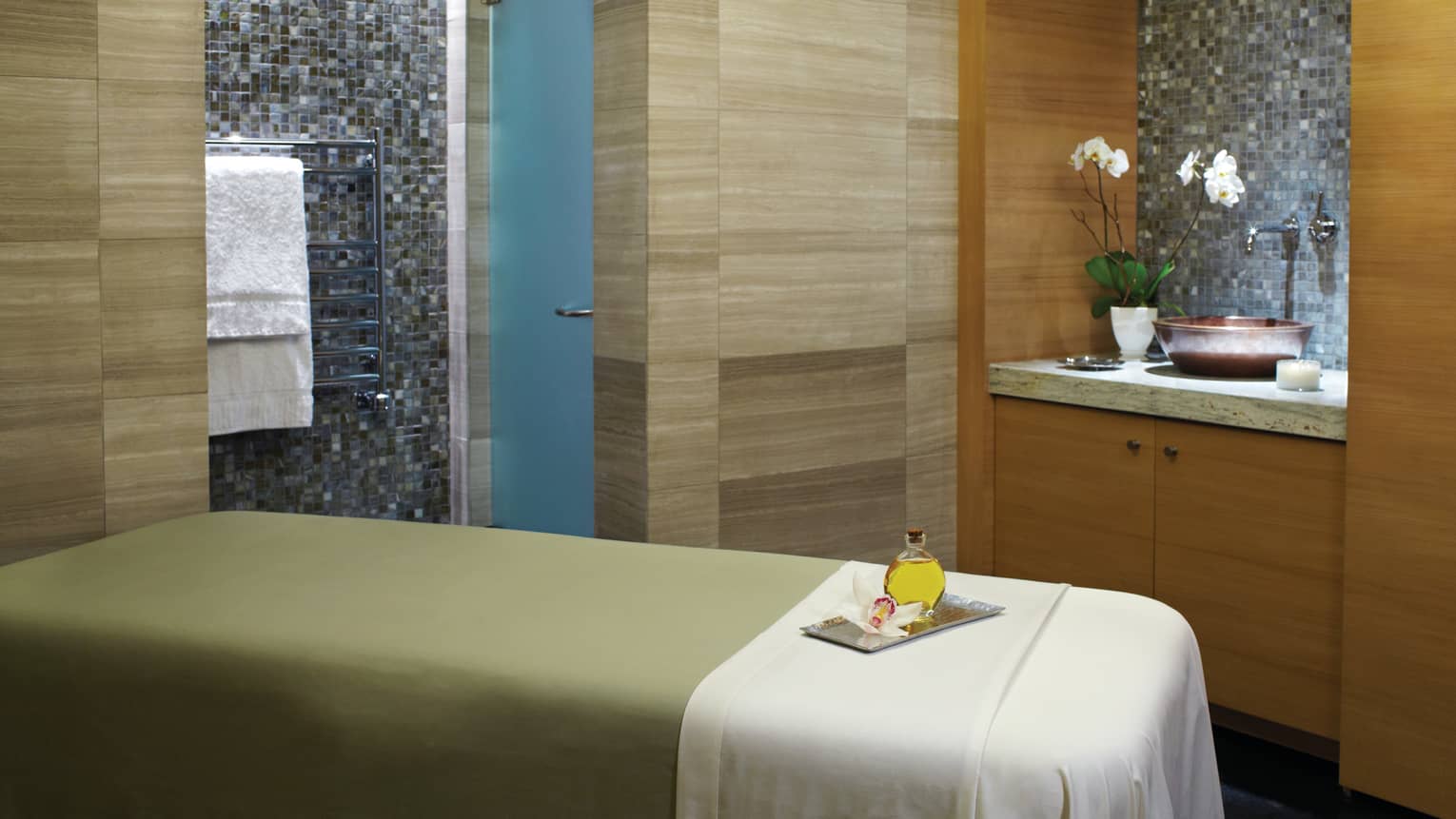 Massage table with green blanket, white sheet, wood and tile walls, sink