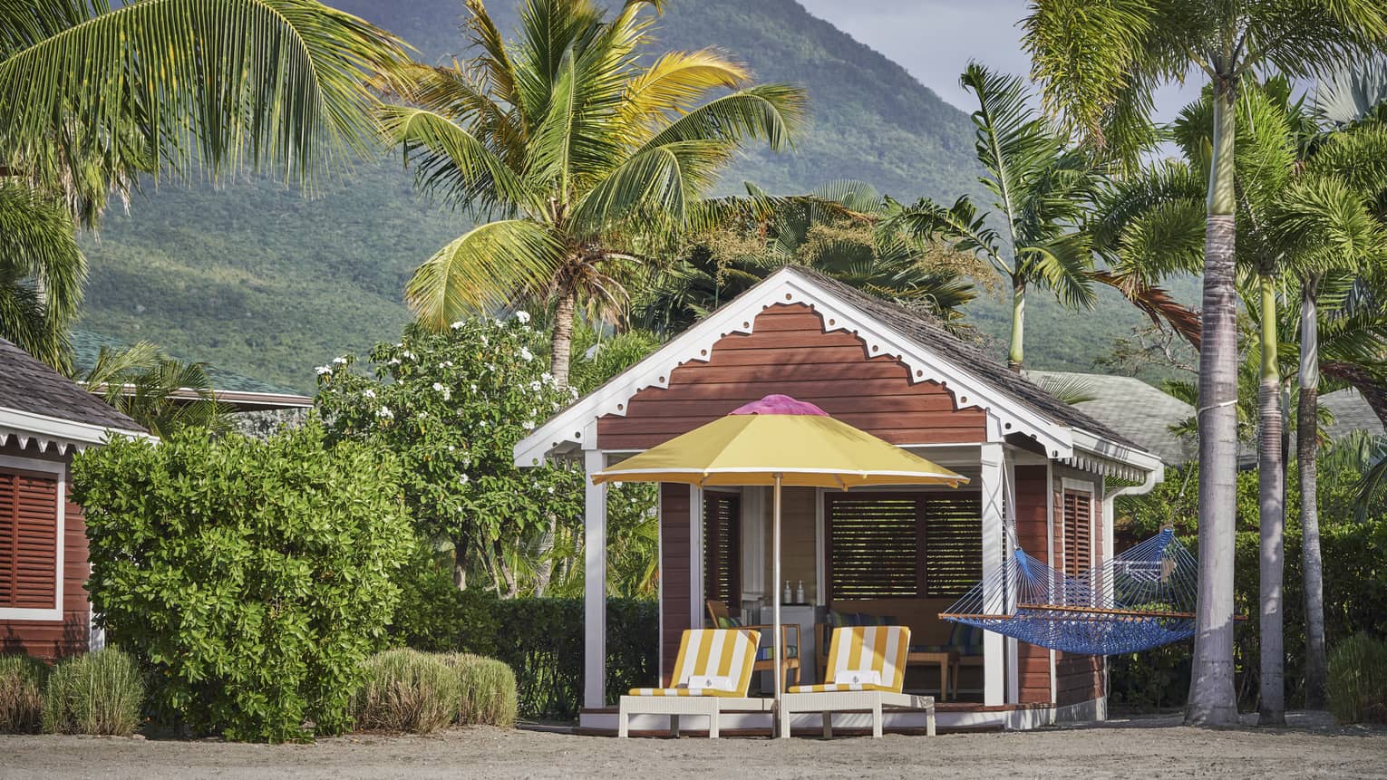 Beach cabana with two patio chairs, umbrella under palm trees