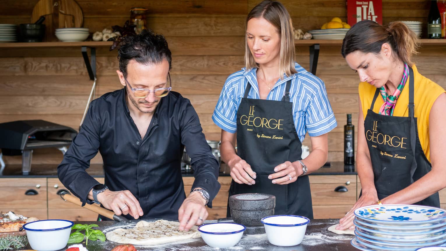 Two women prepare food with chef in outdoor kitchen
