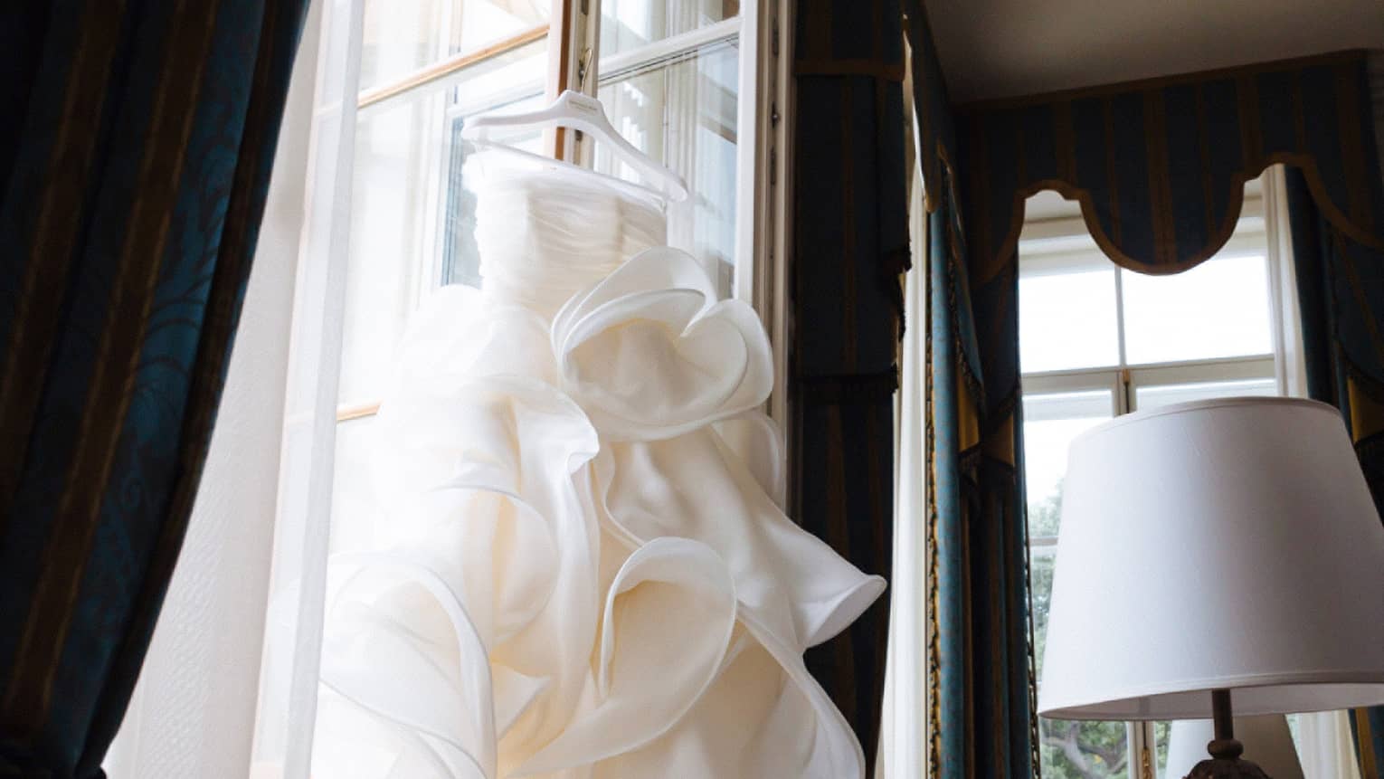 Wedding gown hangs over open window in hotel suite