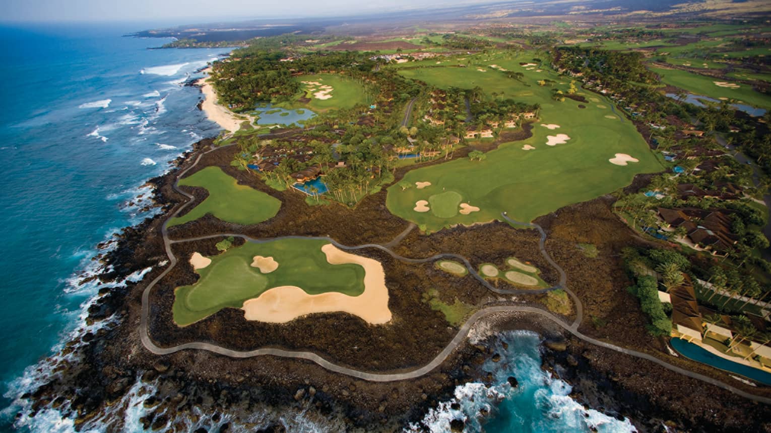 Aerial view of Hualalai Golf Course along rocky shore and ocean