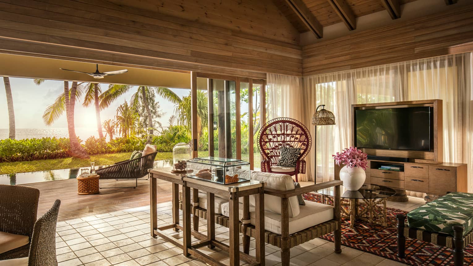Two-bedroom villa living room under wood roof, open-air wall to patio, pool, palms