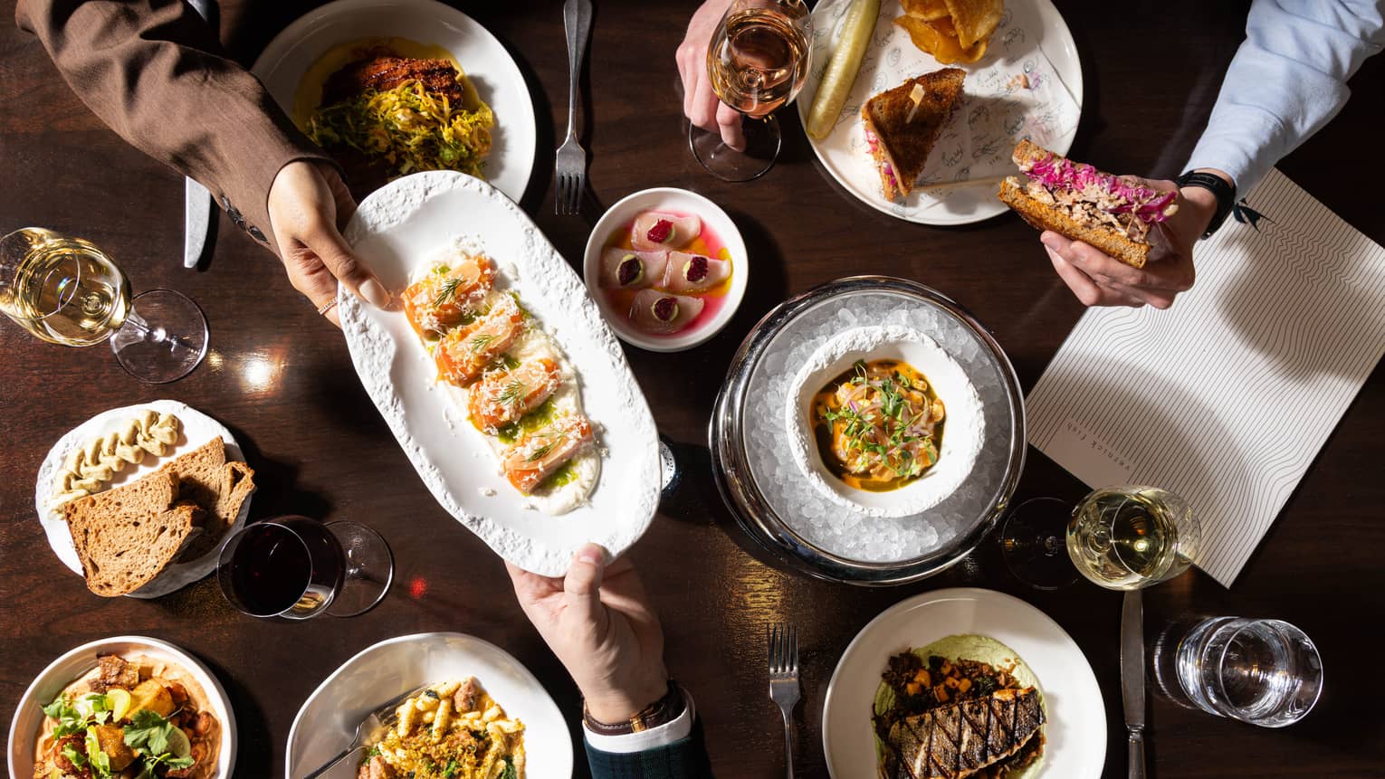 A dark wooden table topped with various colourful culinary dishes and glasses of wine
