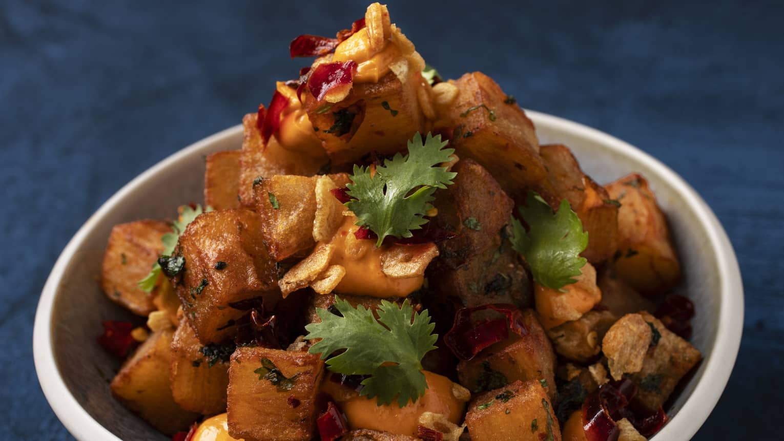 Batata Harra: Crispy layered potatoes with spicy hara coriander dip garnished with cilantro and seved in a white bowl