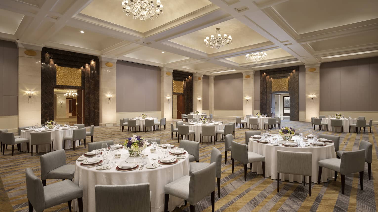 Several round tables set with white table clothes and square chairs.