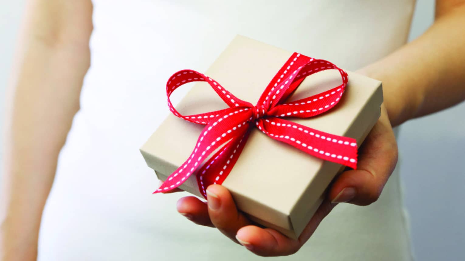 Figure wearing while, holding white gift box tied with red ribbon in a bow