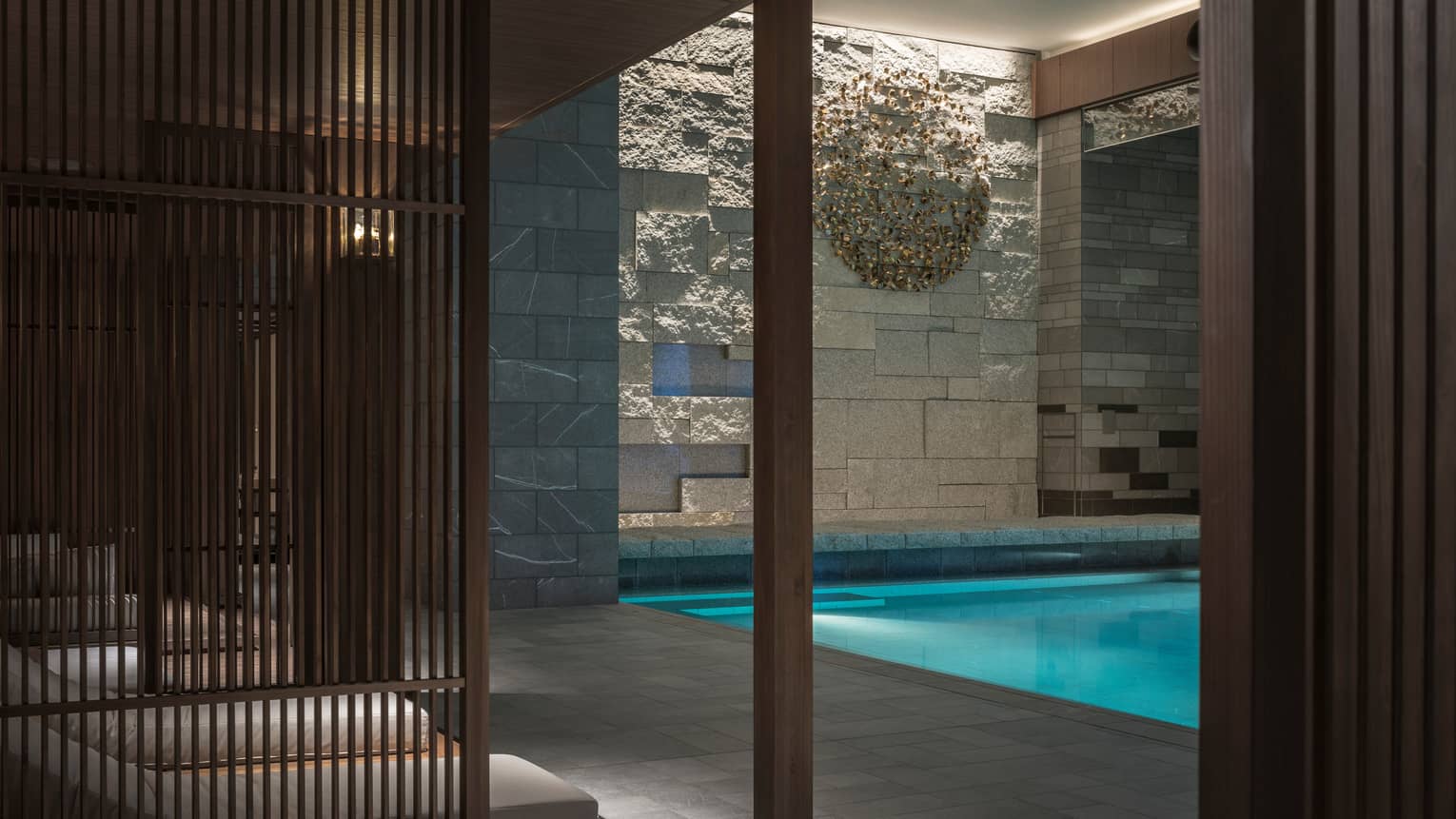 Lounge chairs behind wood wall, by indoor swimming pool under granite rock wall