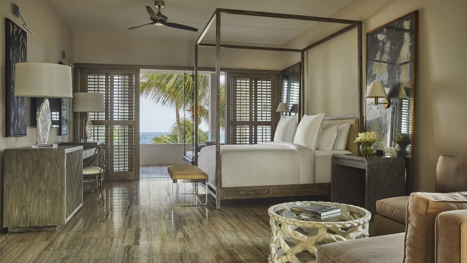 Luxury villa bedroom with a canopy bed, elegant decor, large windows with shutters and a balcony offering ocean and palm tree views