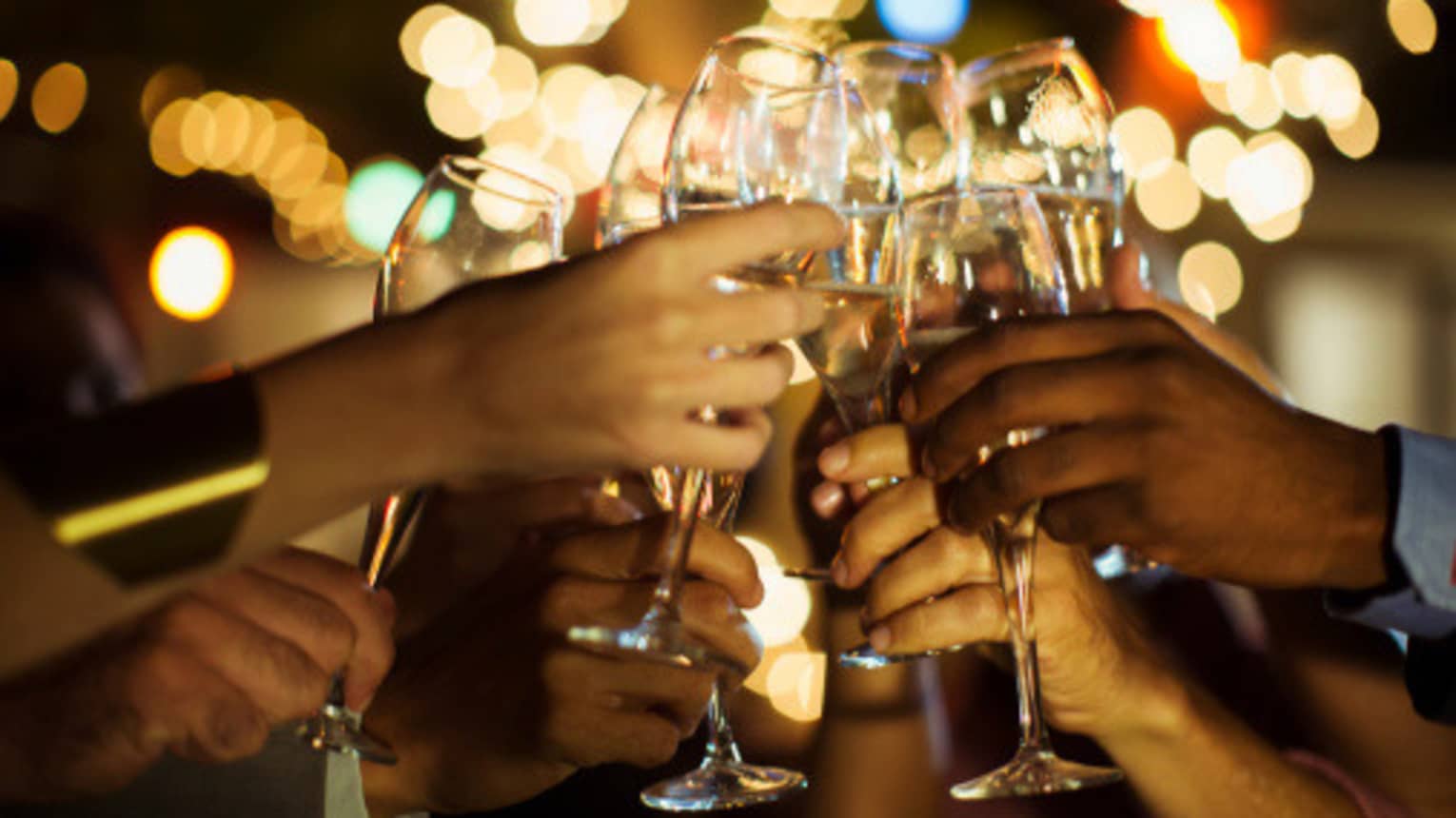 A group of guests clink their glasses of champagne together on a patio with twinkle lights