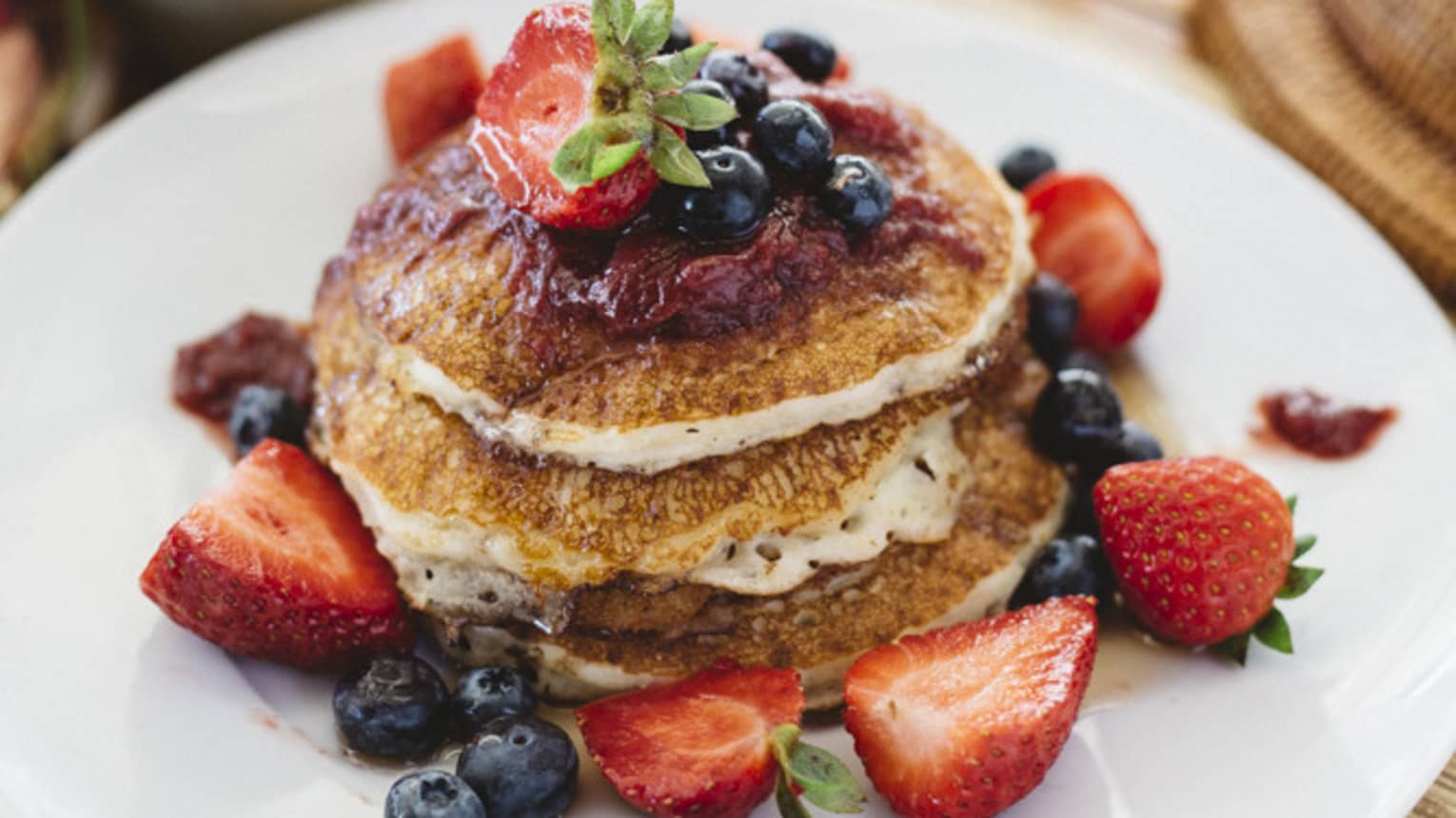 Stack of pancakes with fresh berries on white plate and cup of coffee