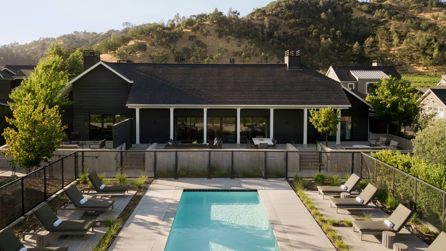Rectangular pool lined with pool loungers and exterior of a three-bedroom private villa in a wine country setting